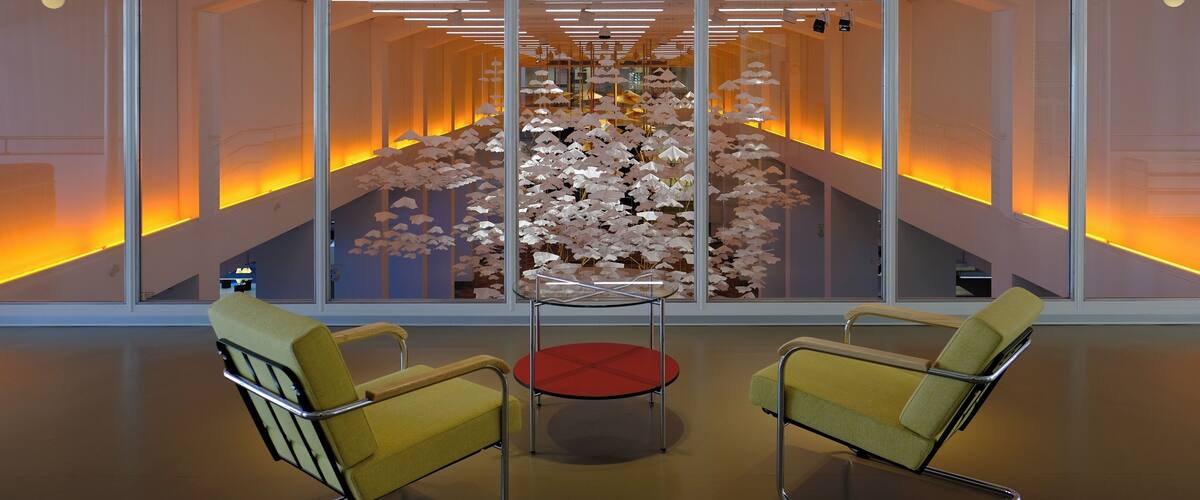A modern interior with yellow chairs, a red table, and a decorative wall with paper flowers.