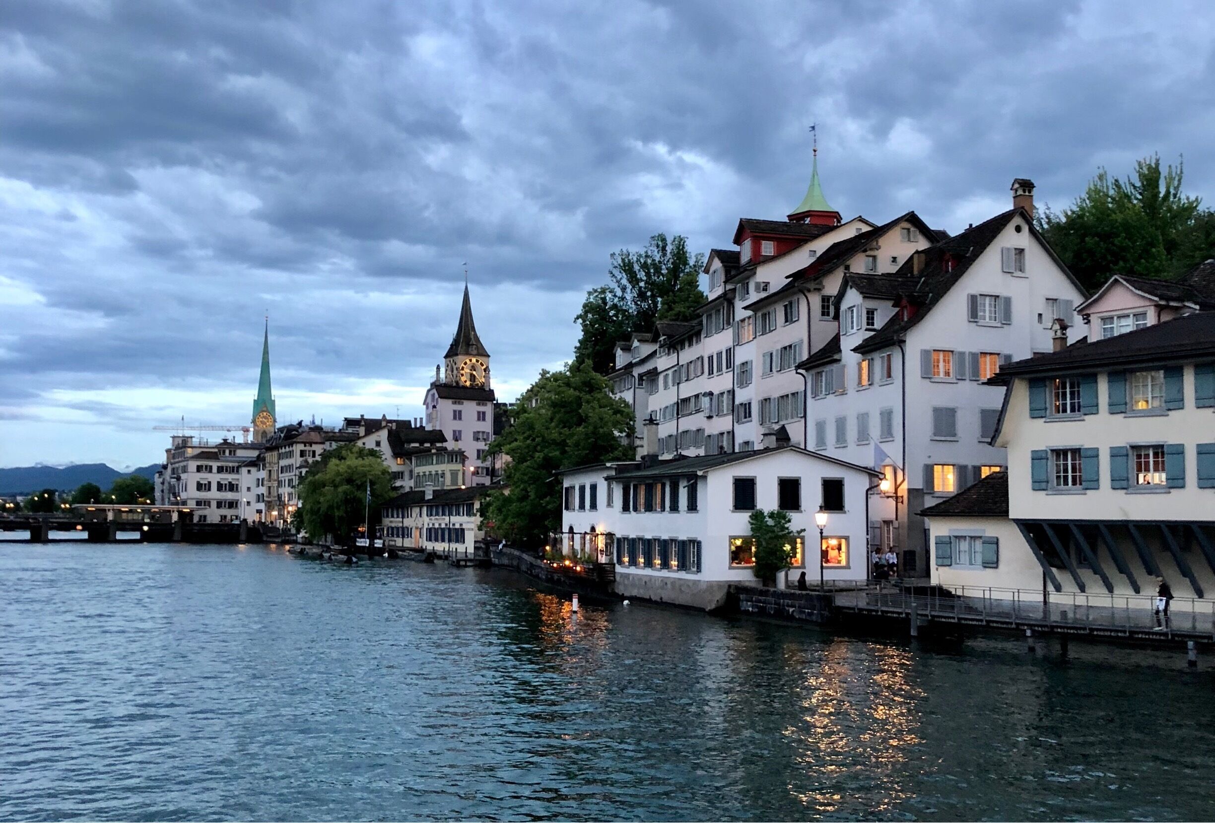 A riverside town with historic buildings, a clock tower, and a bridge.