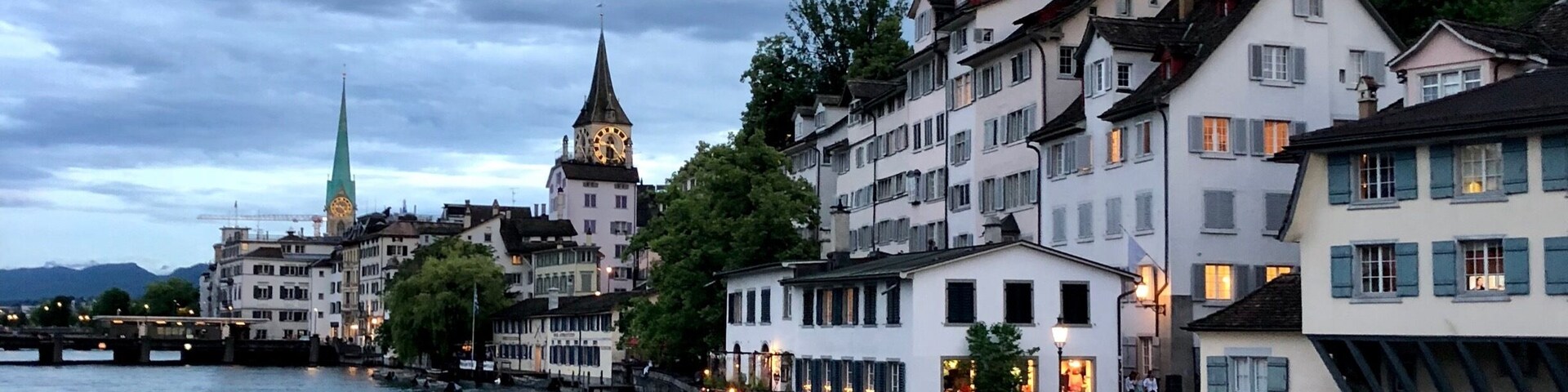 A riverside town with historic buildings, a clock tower, and a bridge.