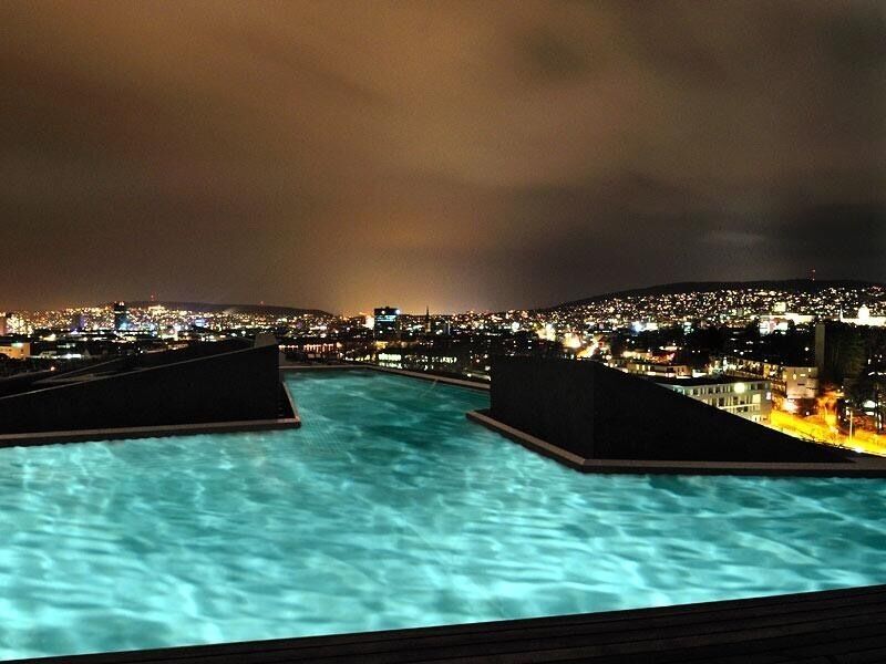 Vista noturna de uma piscina com luzes da cidade ao fundo.
