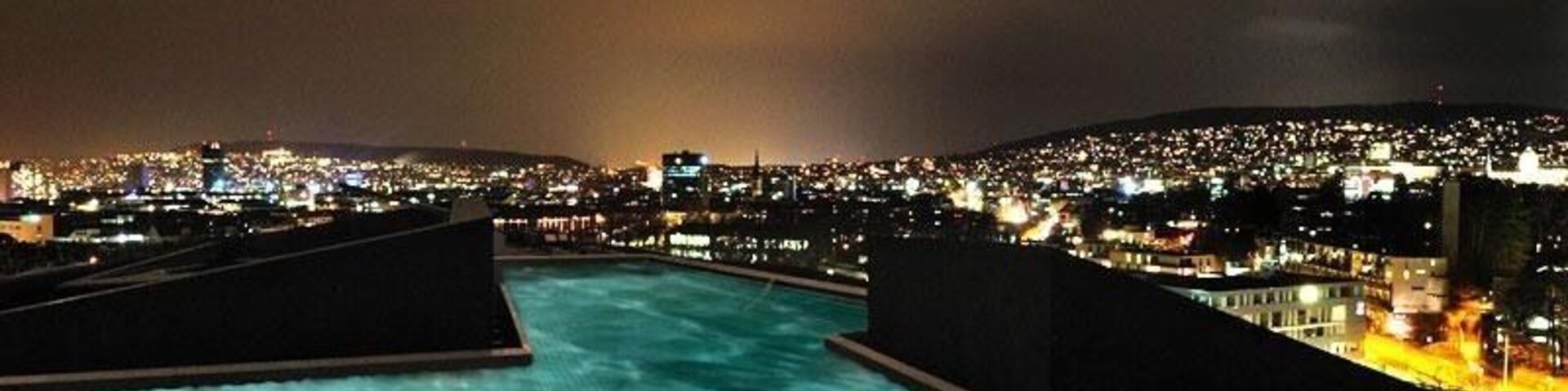 Vista noturna de uma piscina com luzes da cidade ao fundo.