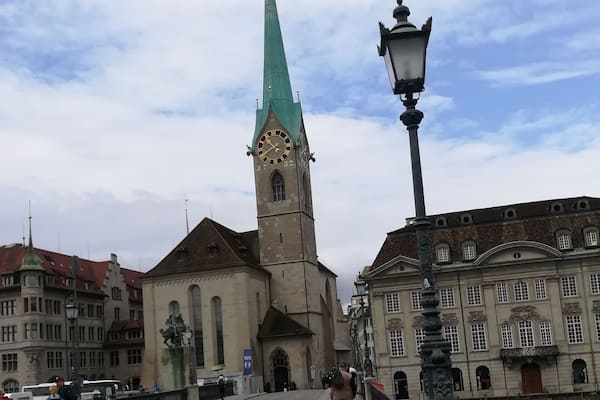 Eine historische Kirche mit einem hohen Turm und einer Uhr, eine Brücke mit Fußgängern und ein Fluss.