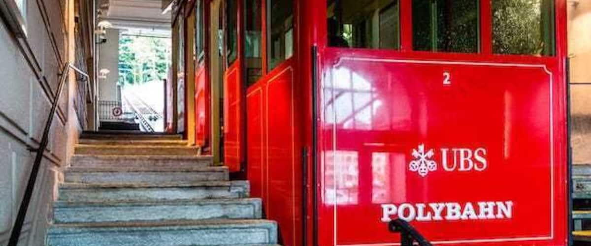 The train at the bottom Polybahn station.
Opened in 1889, The Polybahn, is a funicular railway in the city of Zürich. The line links the Central square with the terrace by the main building of ETH Zürich. 
In 1970 the polybahn closed, and in 1996 was completely rebuilt.
There are 2 stops, with automatic 2 cars on a single track with a passing loop.  The track is 176m long and rises 41m, with an average gradient of 23%.
It takes approx. 100 seconds to travel the distance and runs every 2 to 5 minutes.