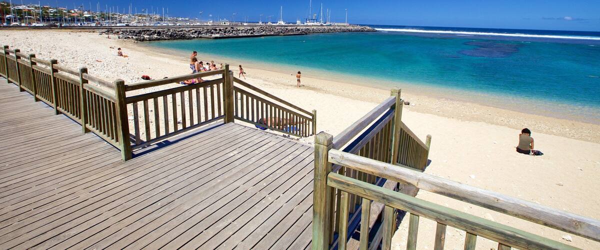 A wooden boardwalk leading to a sandy beach with clear blue water.