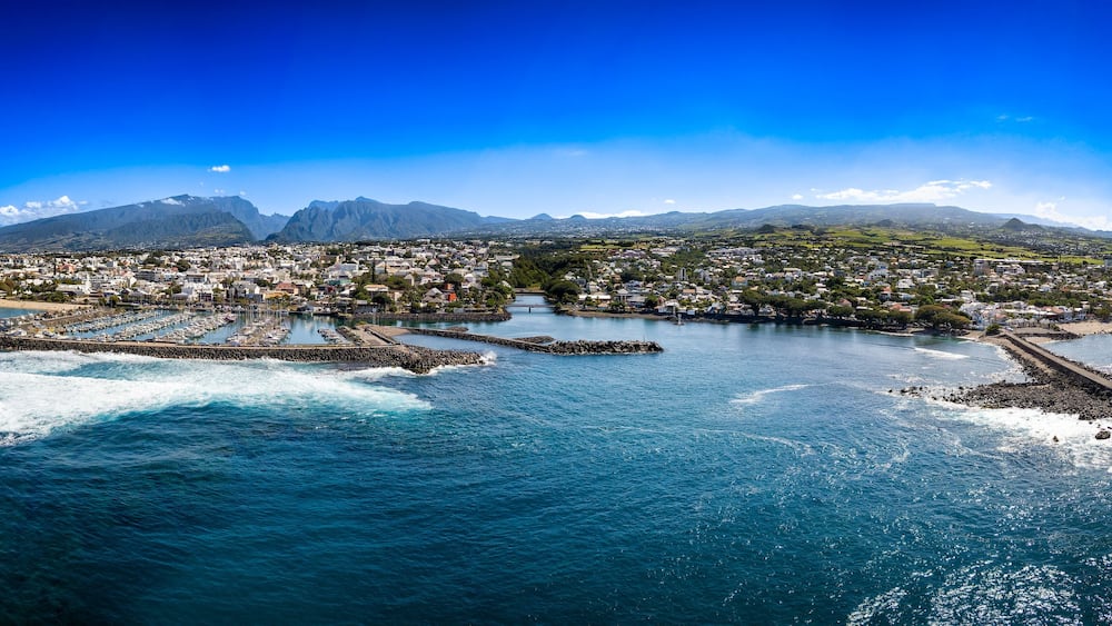 A coastal town with a marina, mountains in the background, and clear blue skies.
