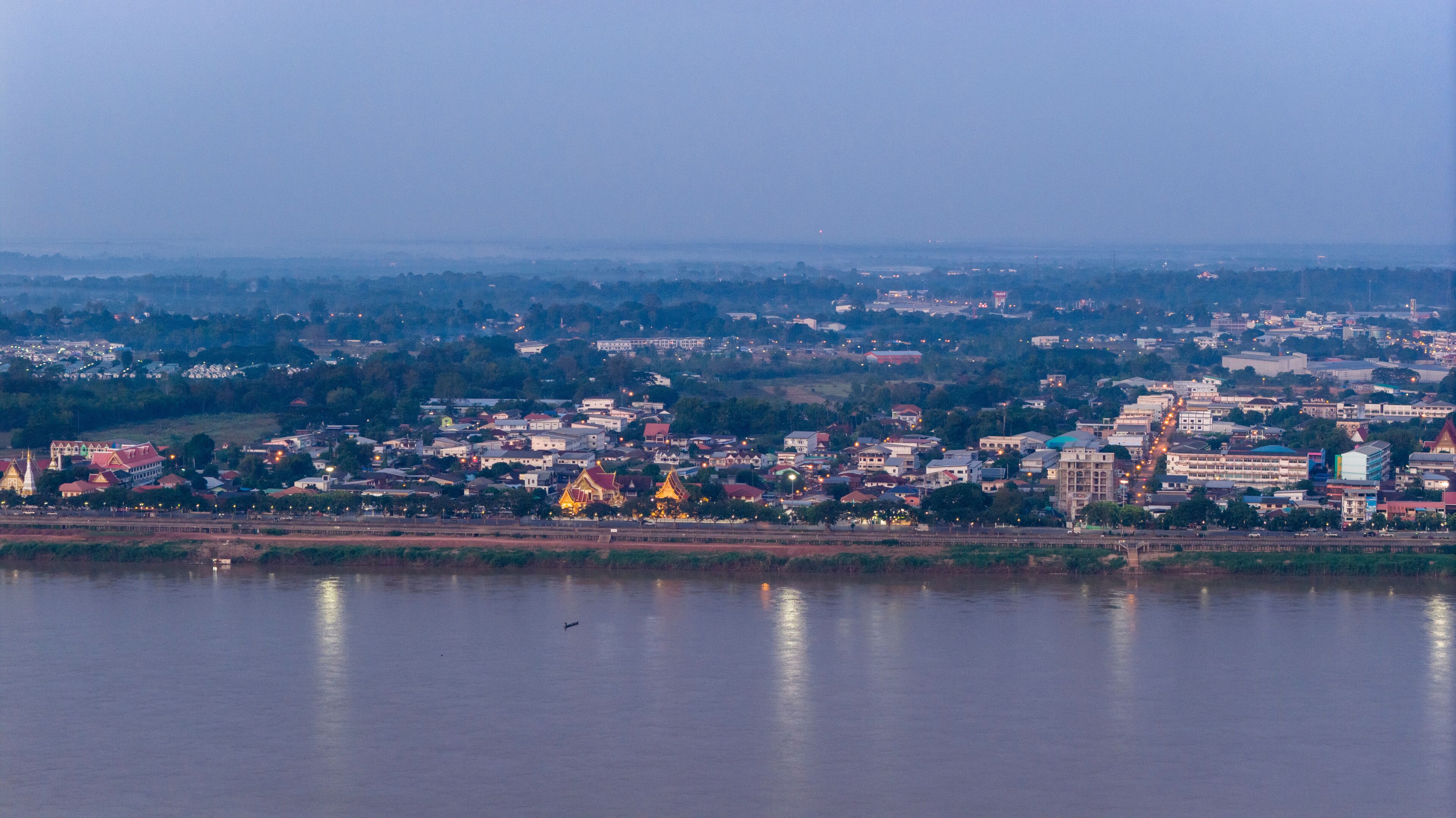 Aerial drone view of Savannakhet city lights turning on at twilight. The street lights illuminate the urban landscape along the Mekong River, highlighting the city layout.