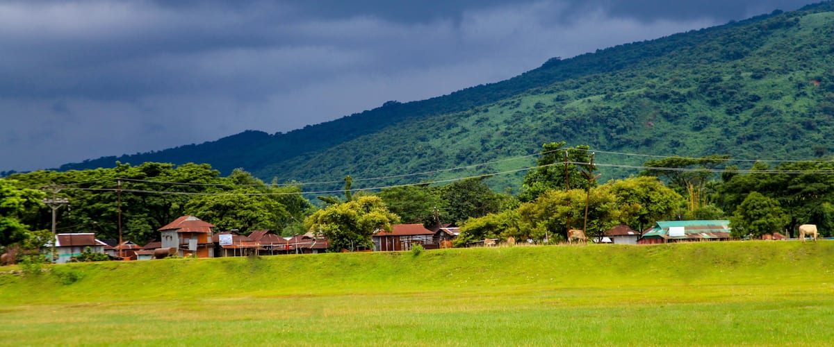 A rural landscape with houses, a green field, and a mountain in the background.