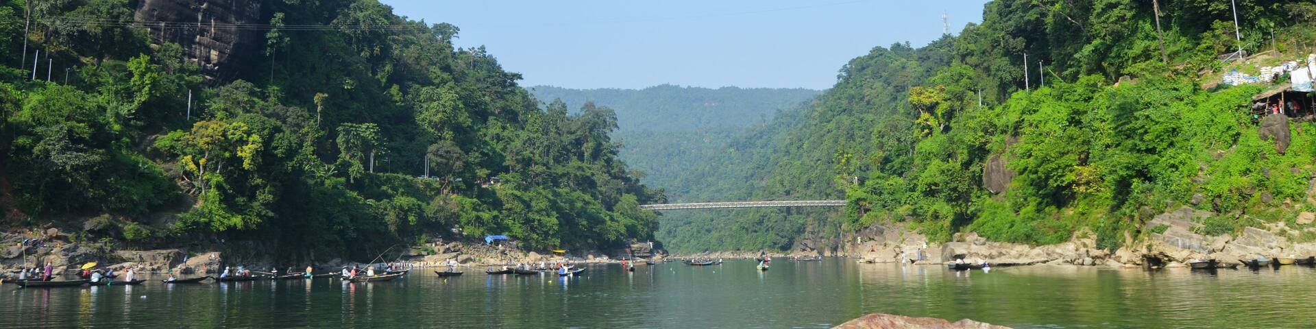 A river flanked by dense green forests and a large rock in the water.