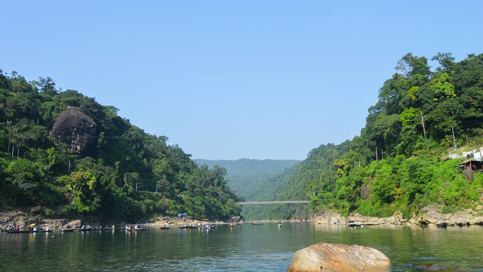 A river flanked by dense green forests and a large rock in the water.