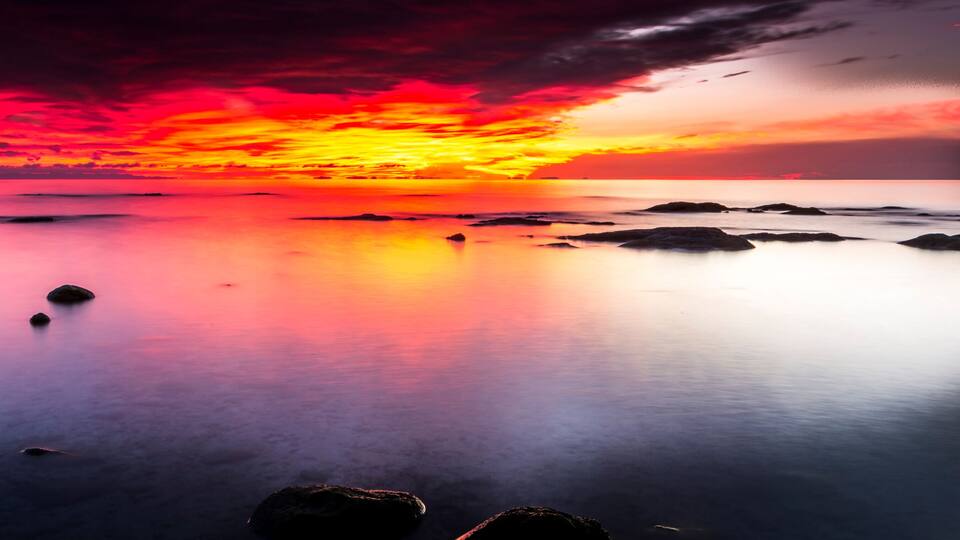 A sunset over a calm sea with rocks in the foreground.