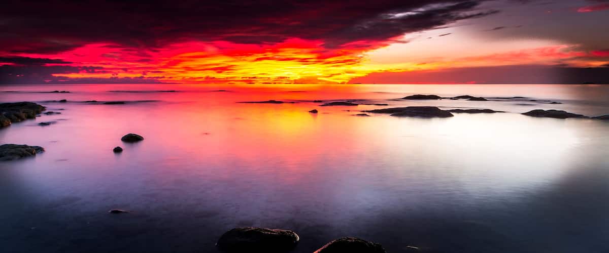 A sunset over a calm sea with rocks in the foreground.