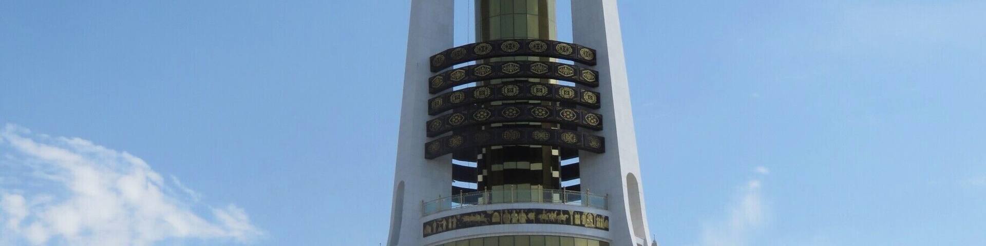 You can see the golden statue of the first president presiding over his children atop the Arch of Neutrality. He is facing the city of Ashgabat, while behind him are the mountains separating Turkmenistan from Iran. The arch of Neutrality confirms Turkmenistan's decision to stay neutral in any conflicts after they left the Soviet Union. You can take a ride up into the tower. Can you see the bottom lift on the right leg of the tower?