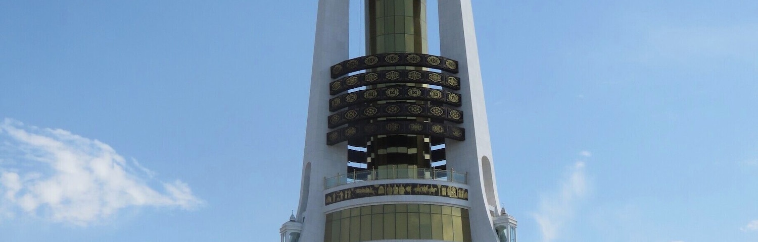 You can see the golden statue of the first president presiding over his children atop the Arch of Neutrality. He is facing the city of Ashgabat, while behind him are the mountains separating Turkmenistan from Iran. The arch of Neutrality confirms Turkmenistan's decision to stay neutral in any conflicts after they left the Soviet Union. You can take a ride up into the tower. Can you see the bottom lift on the right leg of the tower?