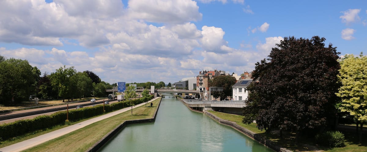 A canal with a bridge, trees, and buildings in the background.