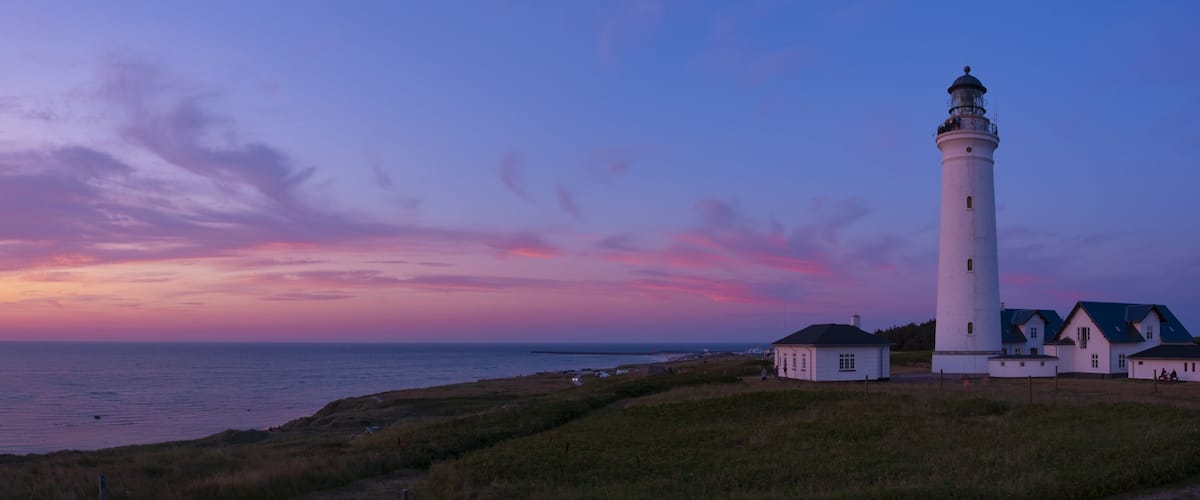 A lighthouse, grassy fields, and a coastal landscape during sunset.