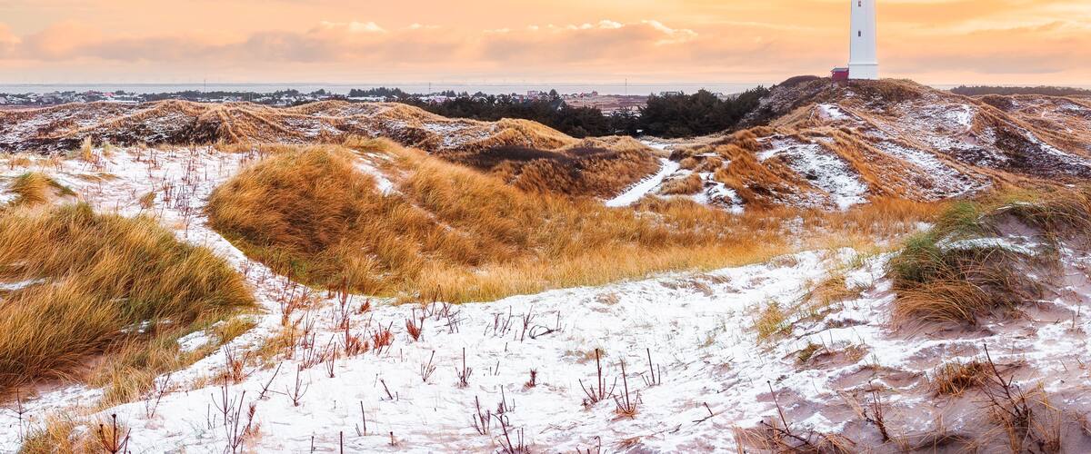 A white lighthouse on a sandy hill with dry grass and snow patches.