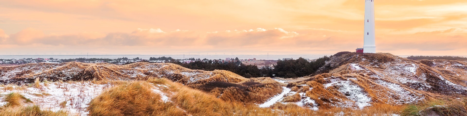 A white lighthouse on a sandy hill with dry grass and snow patches.