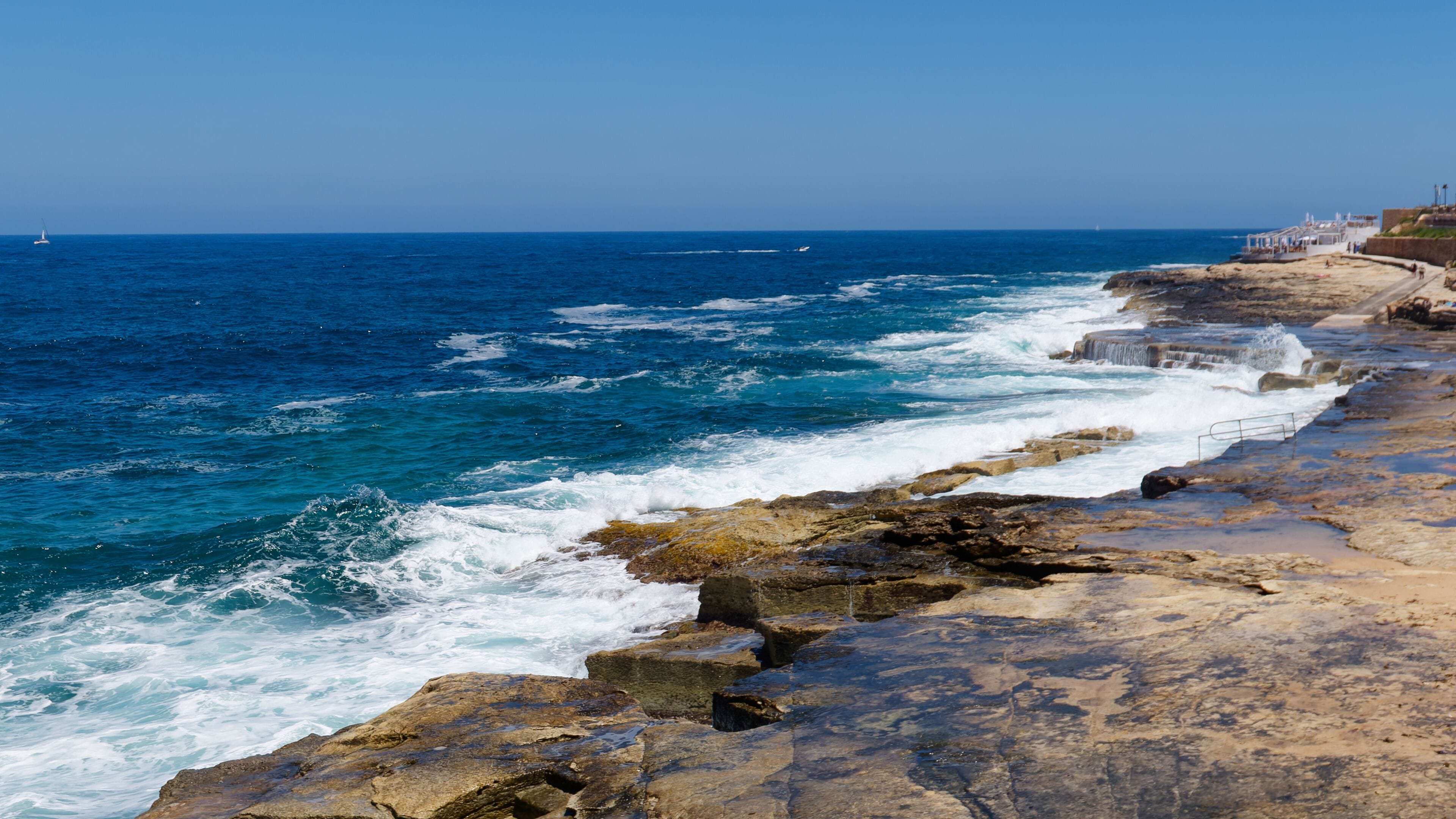 Beautiful turquoise and deep blue sea waves crashing on the flat limestone rock formations, Sliema, Malta