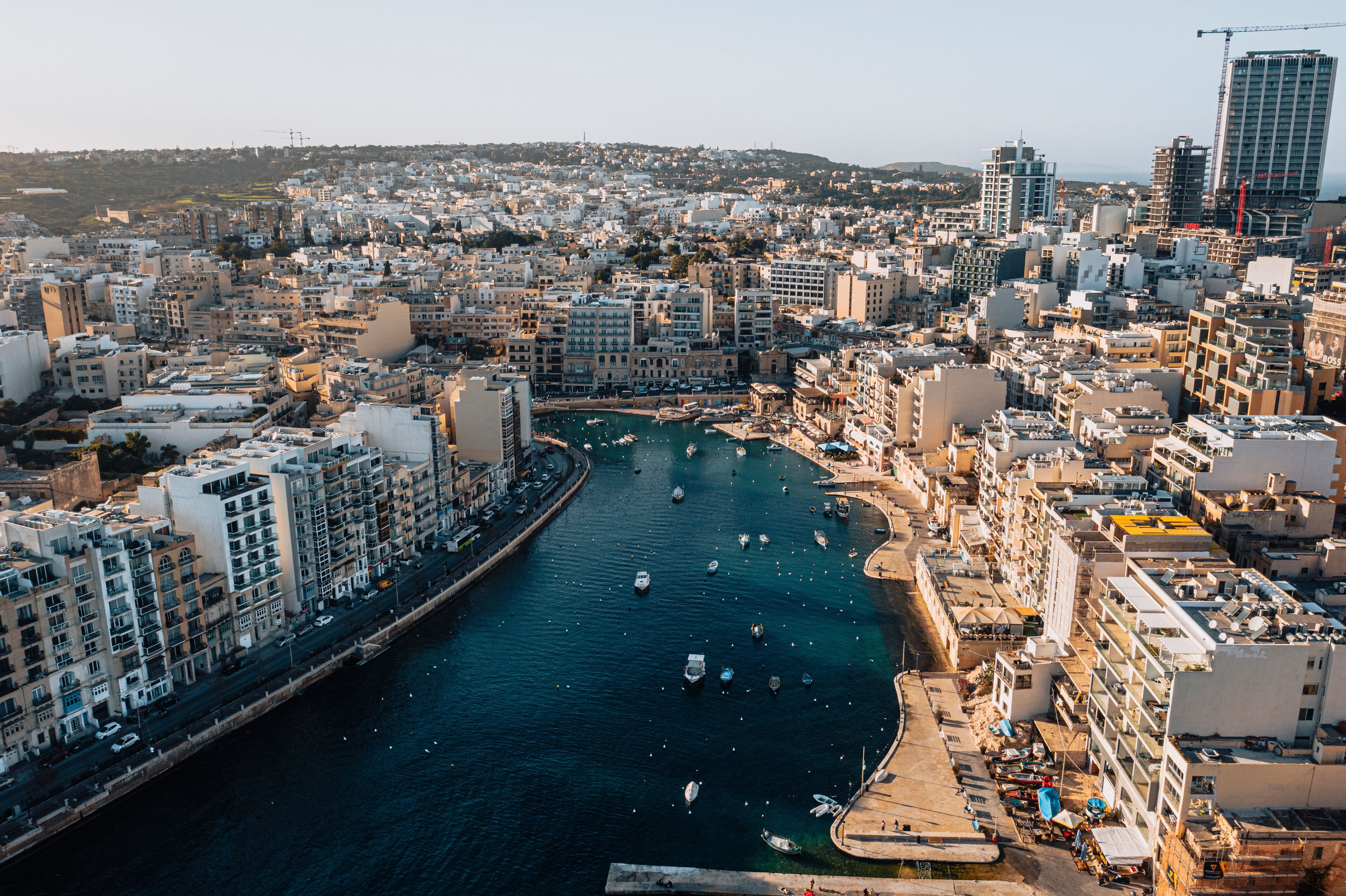 A coastal cityscape with a dense urban area, a marina with boats, and a prominent building under construction.