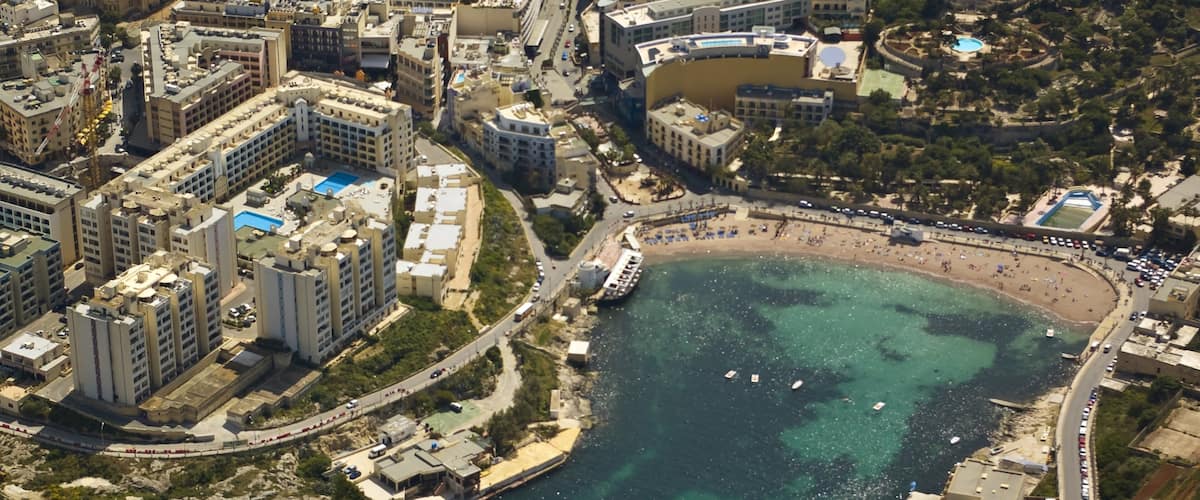 An aerial view of a coastal city with a large beach, dense urban buildings, and a marina.
