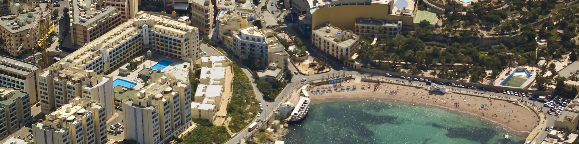 An aerial view of a coastal city with a large beach, dense urban buildings, and a marina.