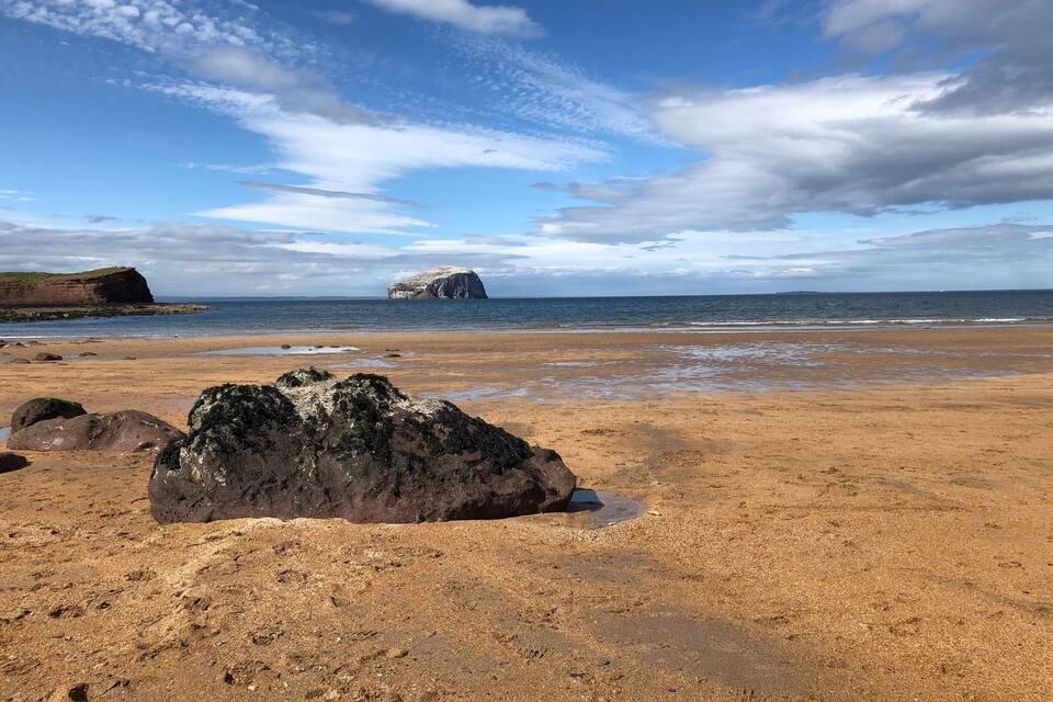 Una playa arenosa con rocas grandes y una isla rocosa distante.