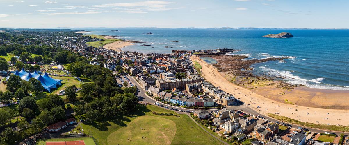 A coastal town with a beach, a large tented area, and a rocky shoreline.