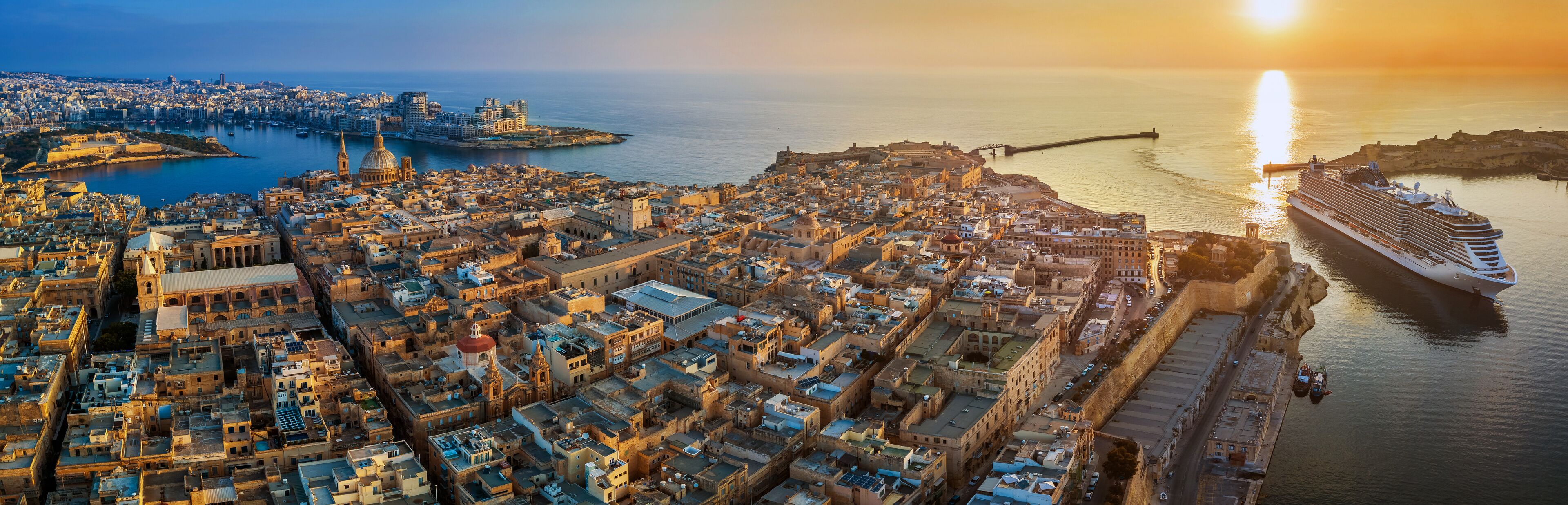 Valletta, Malta - Aerial panoramic view of Valletta with Mount Carmel church, St.Paul's and St.John's Cathedral, Manoel Island, Fort Manoel, Sliema and cruise ship entering Grand Harbor at sunrise