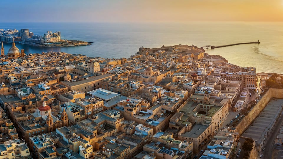 A coastal cityscape with a prominent cathedral, a large cruise ship docked at the port, and a historic fortification.