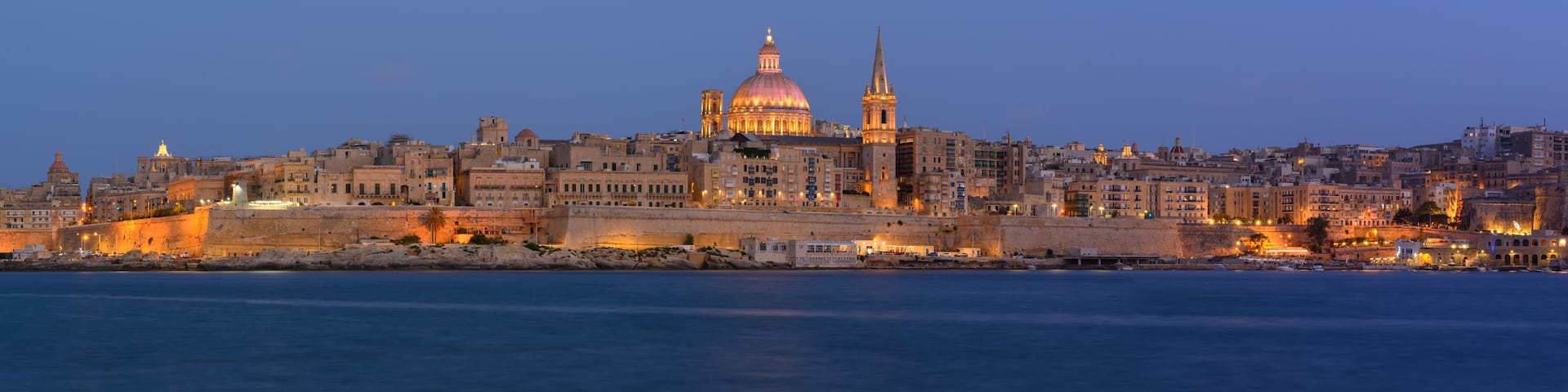 Panoramic view of Valletta Skyline at dusk seen from Sliema Harbour with lights on St. Pauls Cathedral, Malta.