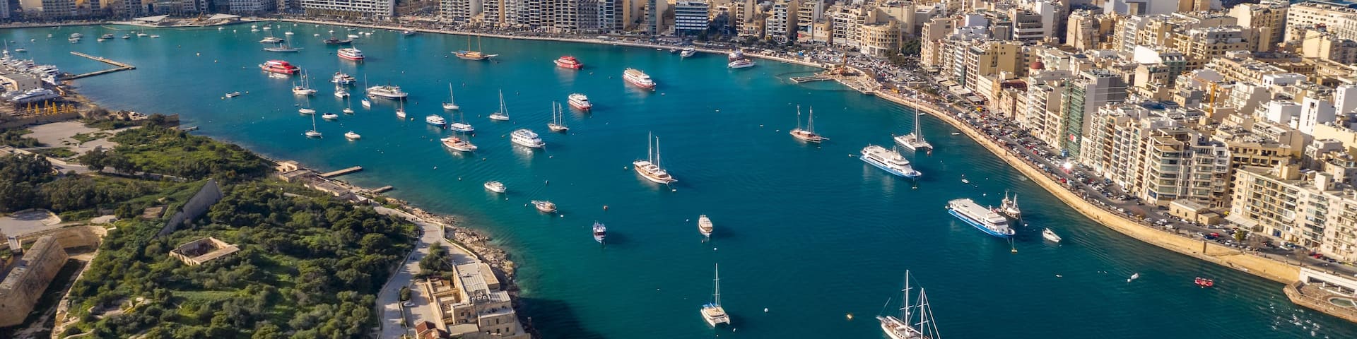 A coastal cityscape with a marina filled with boats, dense urban buildings, and a clear view of the sea.