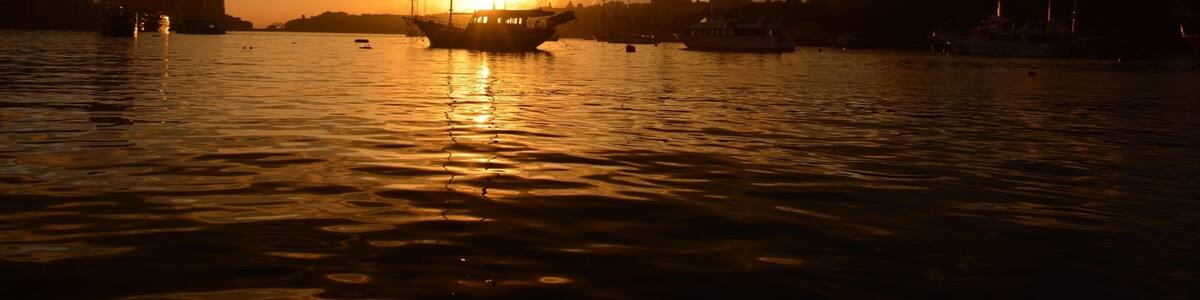 A sunset over a harbor with boats and buildings silhouetted against the sky.