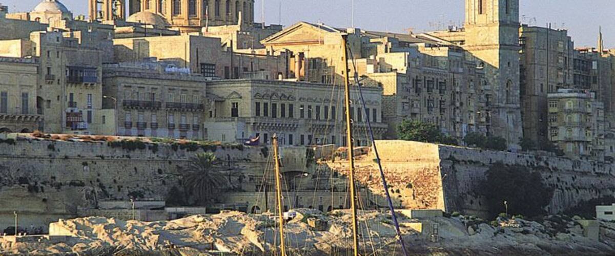 A coastal cityscape with a prominent dome and a tall tower. A sailboat is anchored in the foreground.