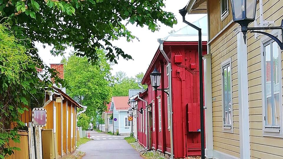 Eine schmale Straße gesäumt von bunten Holzhäusern, ein klarer Himmel und ein Fußweg.