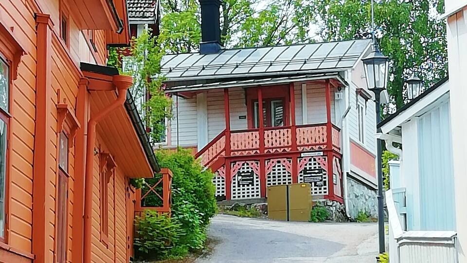 Eine schmale Straße, gesäumt von traditionellen Holzhäusern mit roten und weißen Fassaden, die zu einem Gebäude mit einem roten Balkon führt.