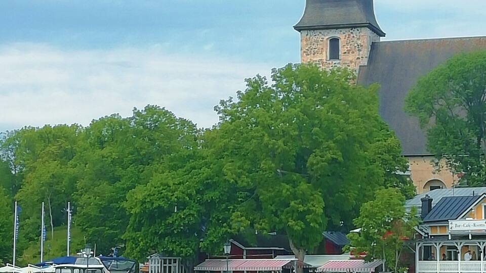 Ein Ufer mit einem Glockenturm, Booten und einer Anlegestelle mit Gebäuden.