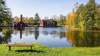 A serene lake with a red barn and a white building in the background, surrounded by autumn foliage.