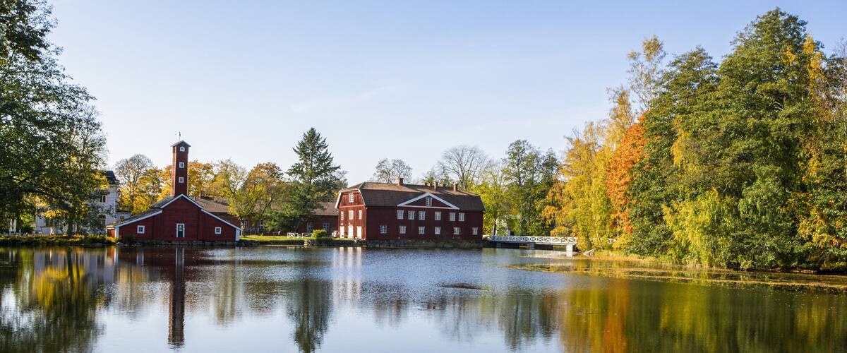 A serene lake with a red barn and a white building in the background, surrounded by autumn foliage.
