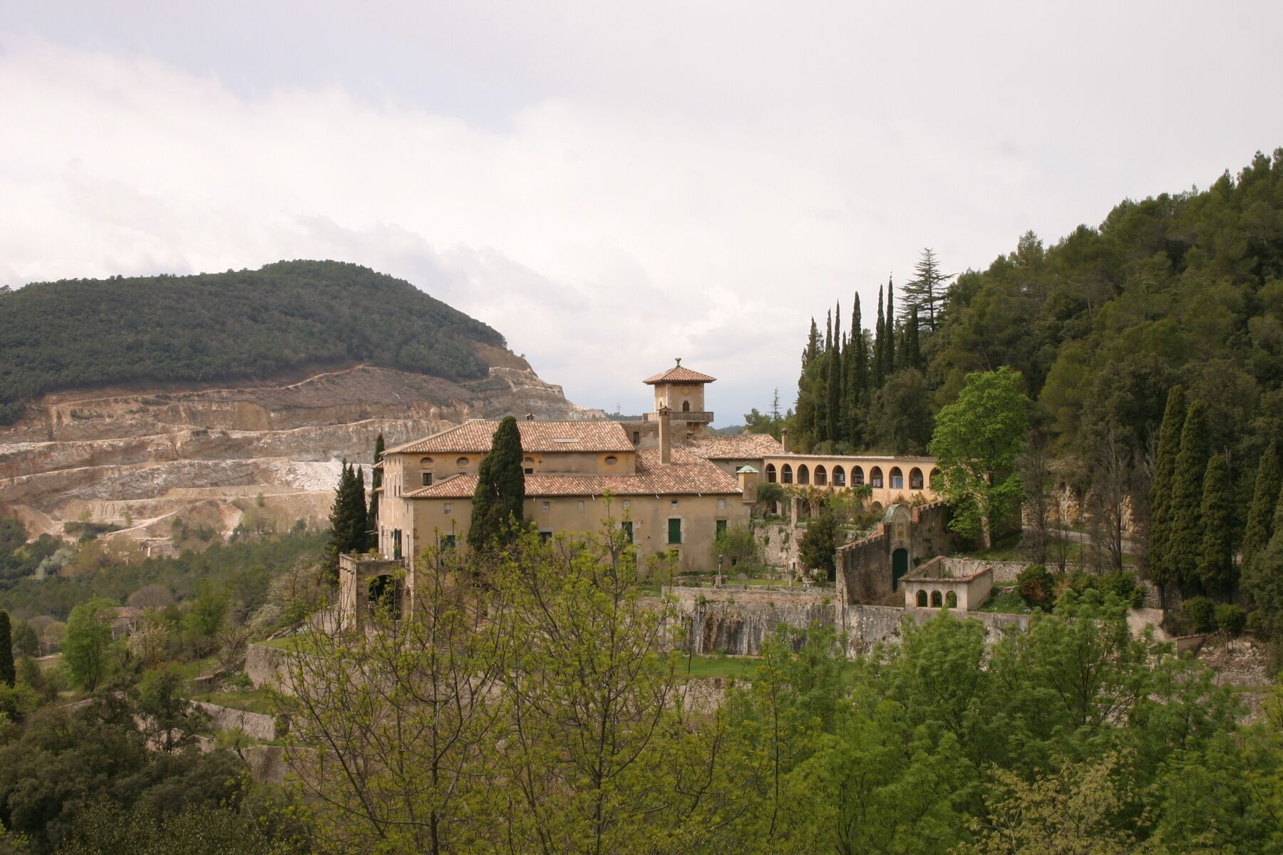 A historic building with a tiled roof, surrounded by trees and a mountainous backdrop.