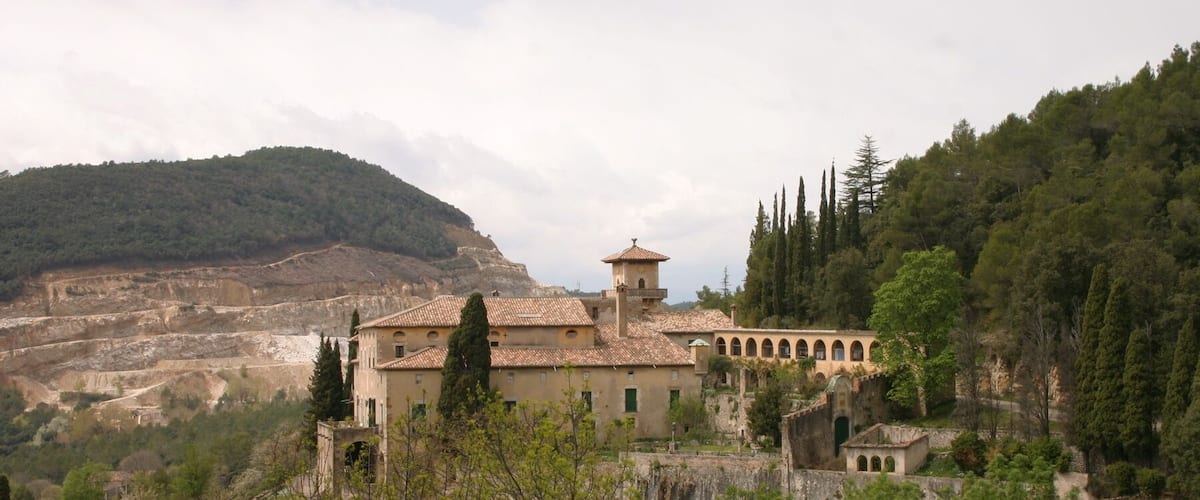 A historic building with a tiled roof, surrounded by trees and a mountainous backdrop.