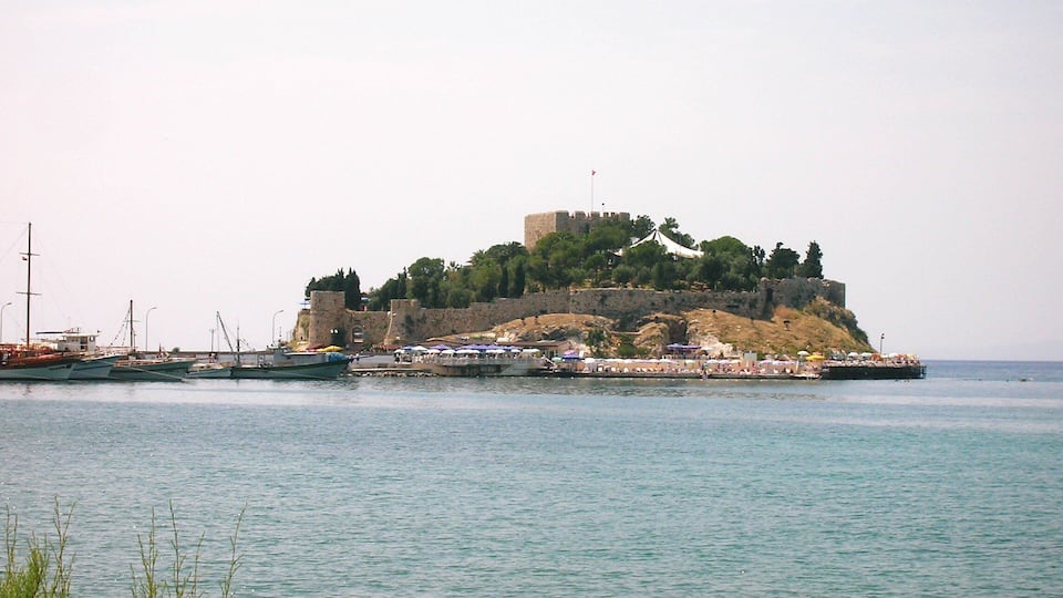 A coastal fortification with a tower, surrounded by water and boats.