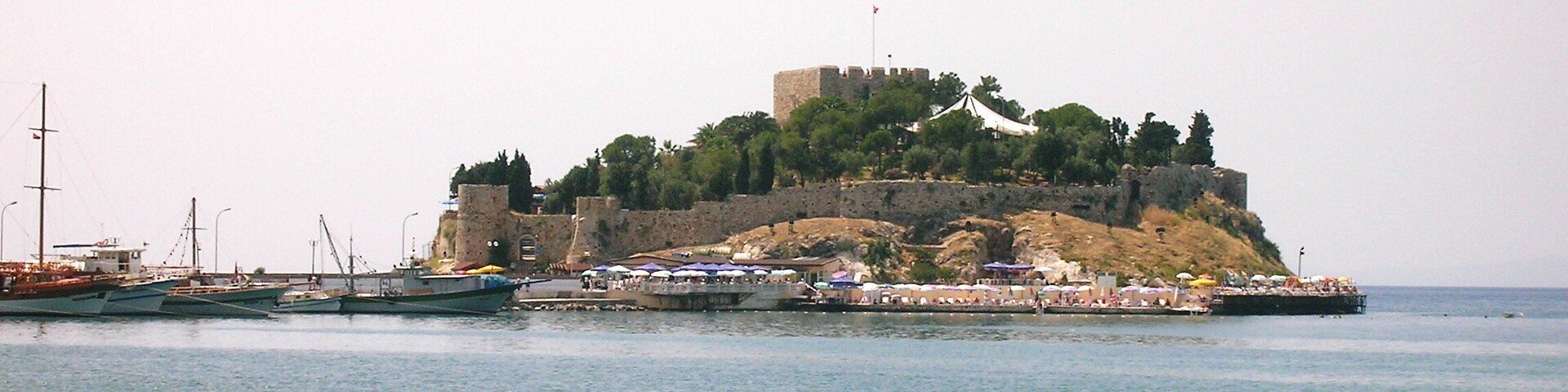 Una fortificación costera con una torre, rodeada de agua y barcos.