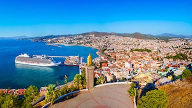 A coastal cityscape with a cruise ship docked at a pier, surrounded by densely packed buildings and a mountainous backdrop.