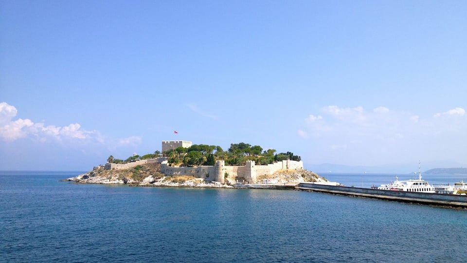 A coastal fortification with a flag on top, surrounded by water and a clear sky.