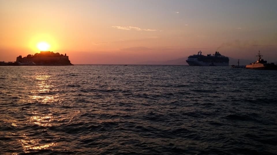 A sunset over a body of water with a cruise ship and a military vessel.