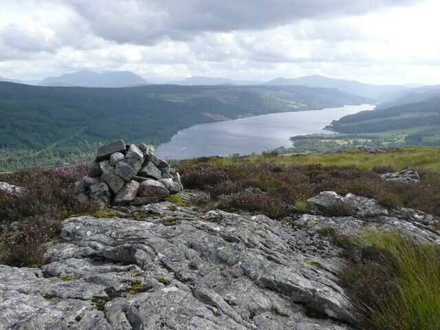 Um afloramento rochoso com um monte de pedras, um lago e colinas ondulantes ao fundo.