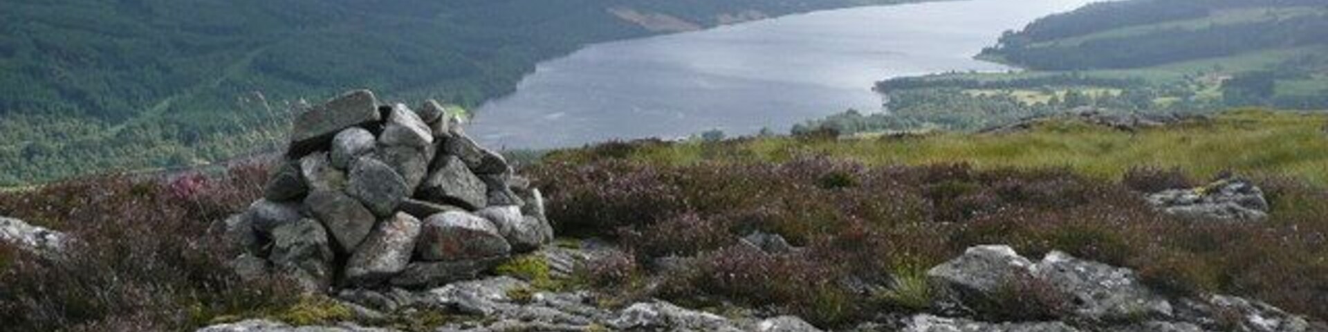 Um afloramento rochoso com um monte de pedras, um lago e colinas ondulantes ao fundo.