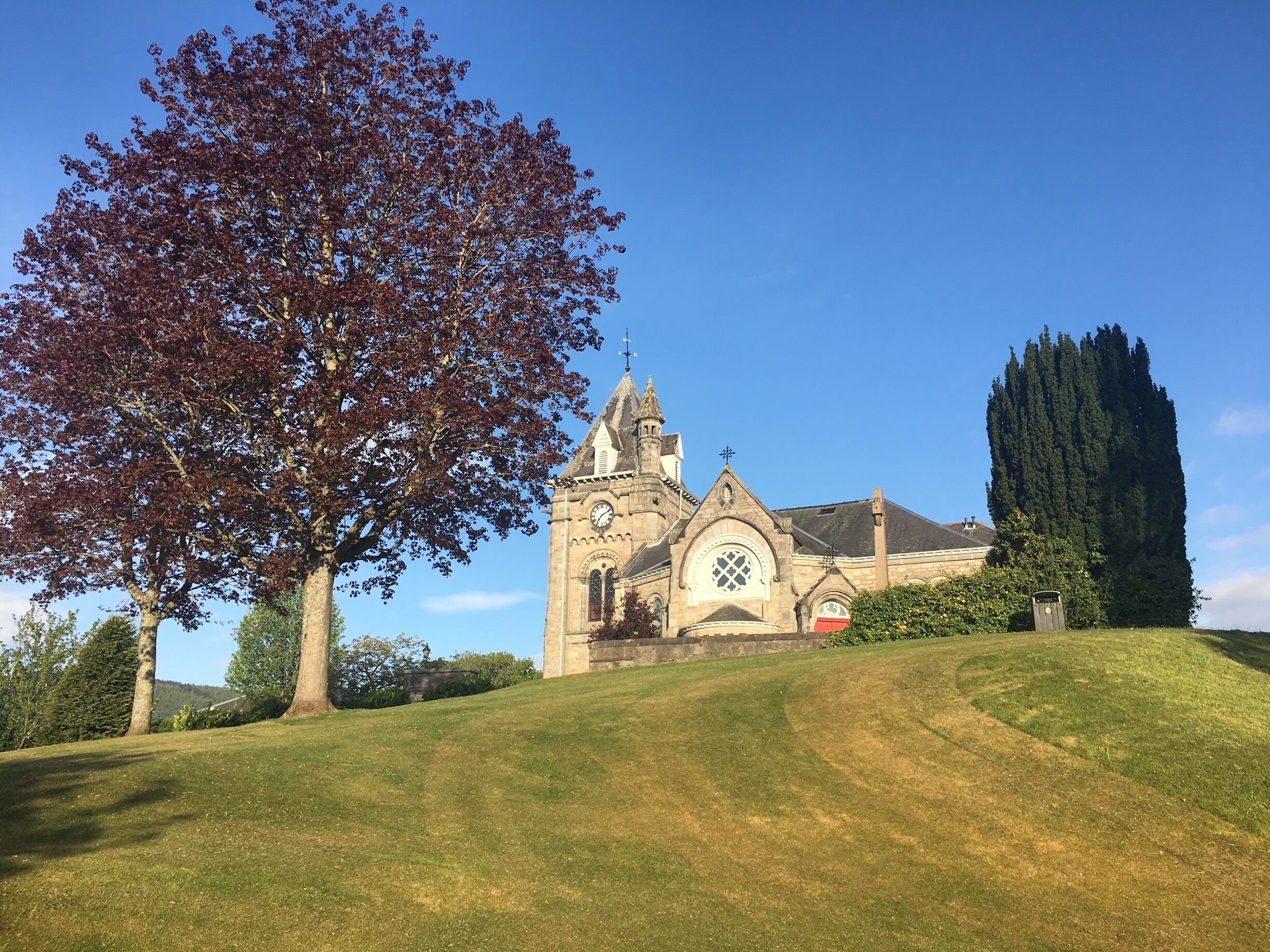 A church with a clock tower, surrounded by a grassy hill and trees.