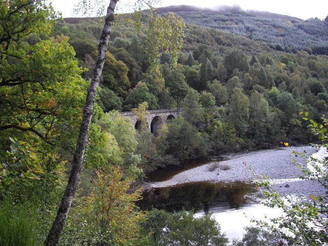 A stone bridge over a river surrounded by dense forest and hills.