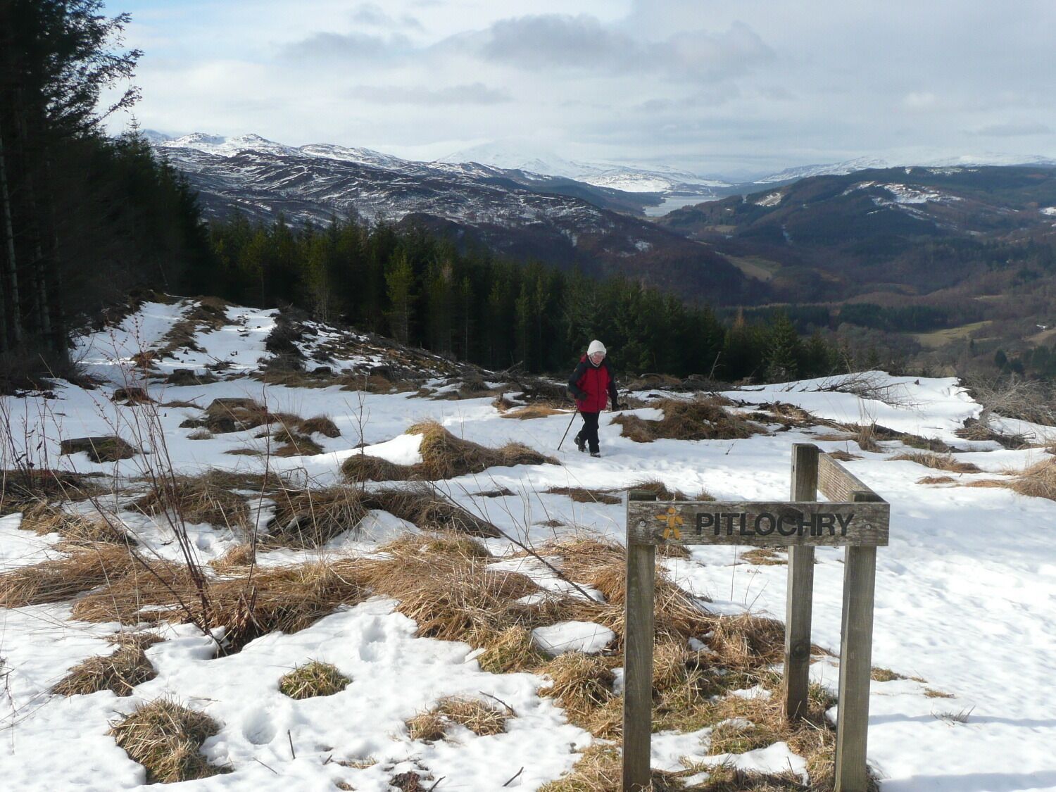 A person hiking in a snowy landscape with a sign reading "Pitlochry".